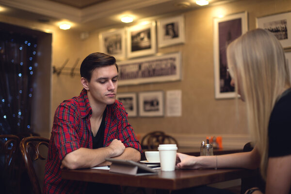 Two friends hipster man young woman are sitting in front of each other the cafe and chat with a cup coffee