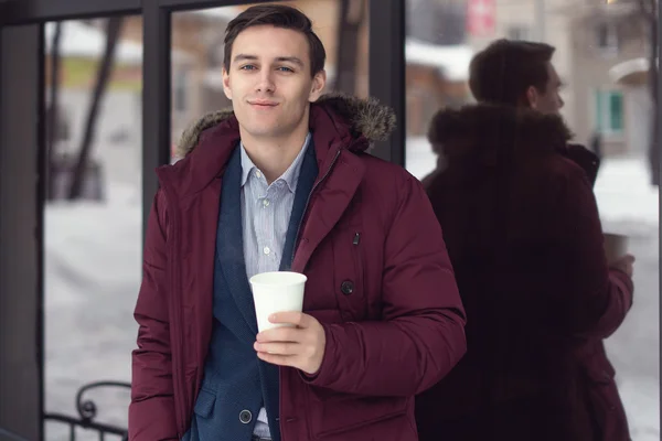 Jovem empresário de casaco de inverno leva café para ir a um café . — Fotografia de Stock