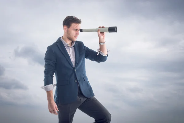 Joven atractivo hombre de negocios guapo de pie con nubes alrededor y mirando a través del catalejo para encontrar nuevas perspectivas . — Foto de Stock