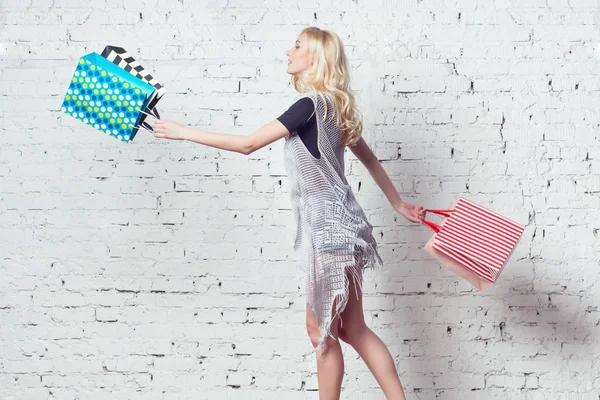 Удивительная блондинка идет по магазинам с парой разноцветных сумок в руках . — стоковое фото