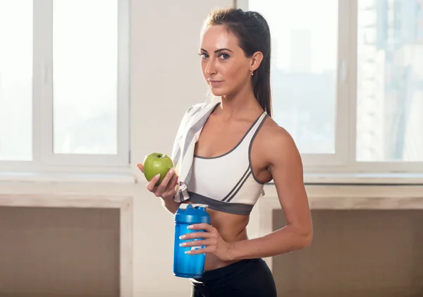 Preciosa joven atlética deportiva mujer en traje deportivo sosteniendo manzana y agitador azul después del entrenamiento . — Foto de Stock