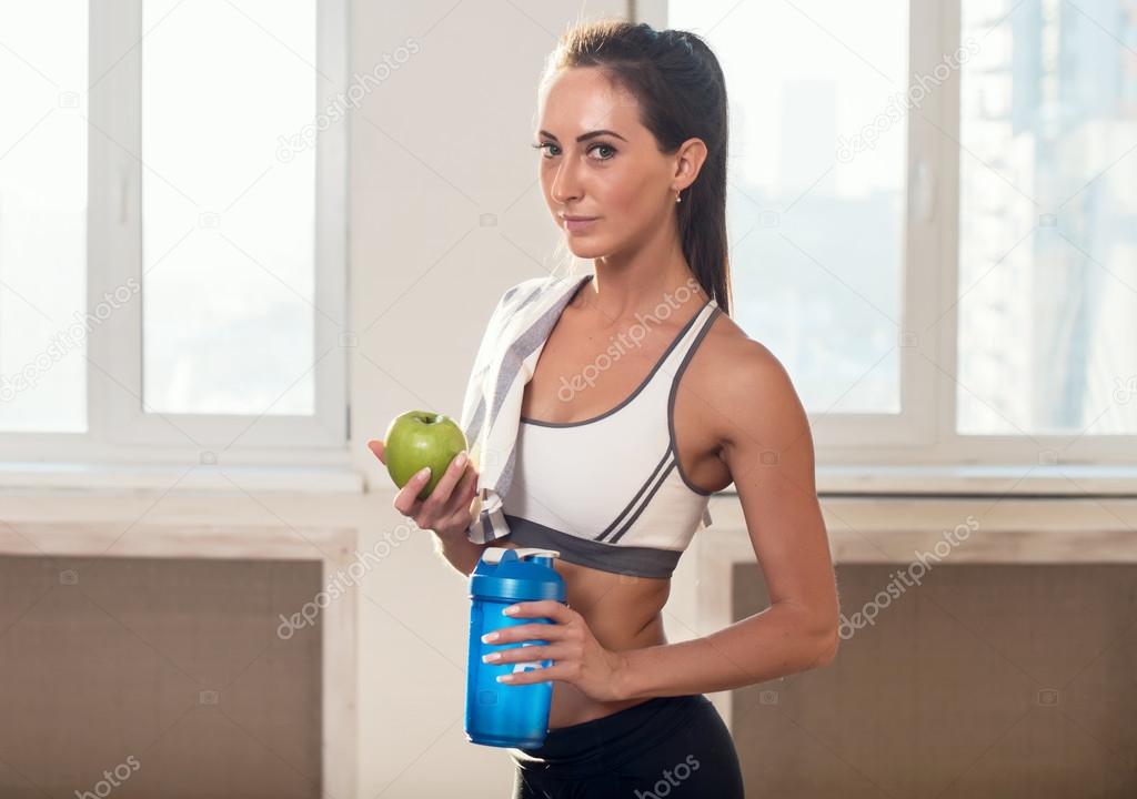 Gorgeous young athletic sportive woman in sport outfit holding apple and blue shaker after the training.