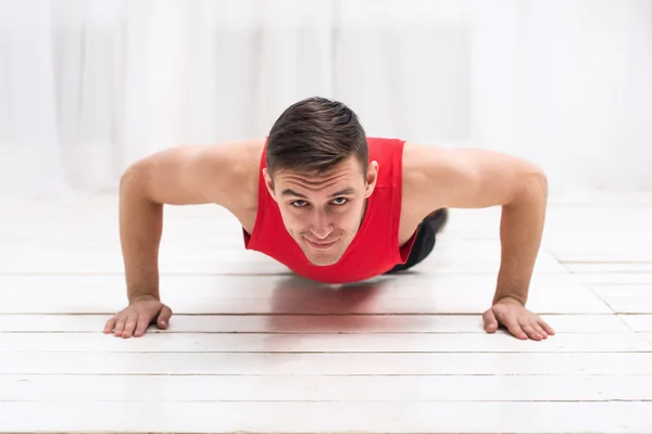 Empujones. Entrenamiento de un joven atractivo en camiseta roja en el gimnasio de piso de madera blanco o en casa —  Fotos de Stock