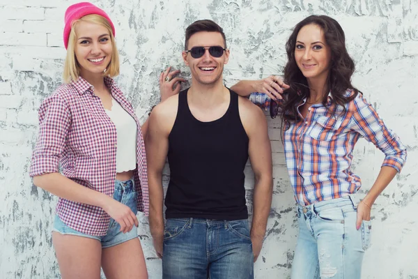 Amigos duas meninas bonitas e cara bonito de pé perto de um sorriso de parede alegremente . — Fotografia de Stock