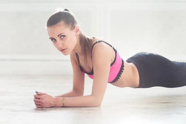 Slim fitnes chica joven con cola de caballo haciendo ejercicio de planchado en el interior de la gimnasia en casa —  Fotos de Stock