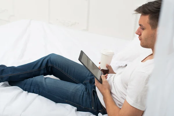 Vista lateral de un hombre casual en la cama en casa navegar por Internet y beber café —  Fotos de Stock