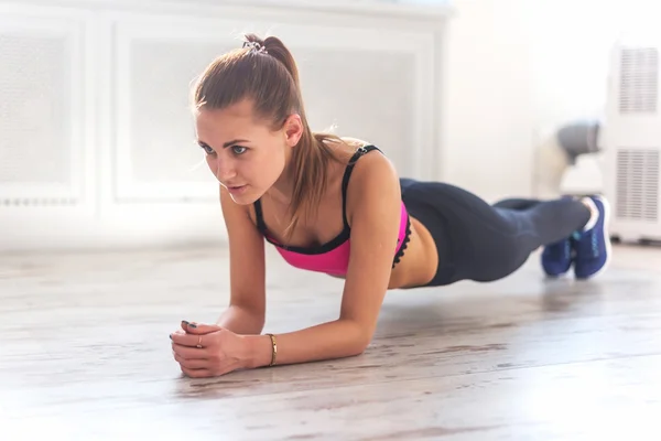 Kapalı ev jimnastik, planking egzersiz yaparak at kuyruğu ince fitnes genç kızla