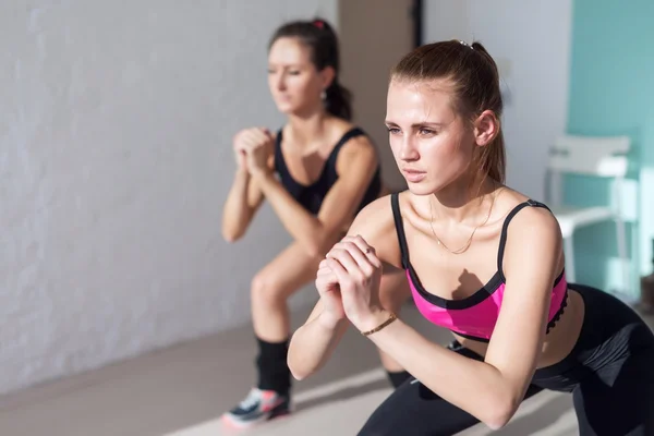 Duas meninas fazendo agachamentos juntos dentro de casa treinamento de aquecimento no ginásio fitness, esporte e estilo de vida conceito — Fotografia de Stock