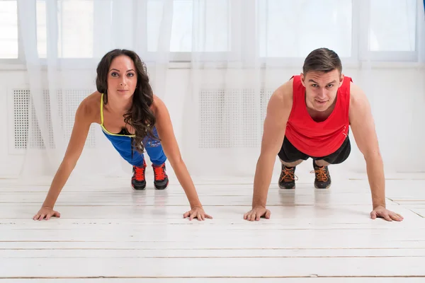 Entrenamiento. Deportiva chica y chico de entrenamiento juntos haciendo flexiones en el piso de madera blanca . — Foto de Stock