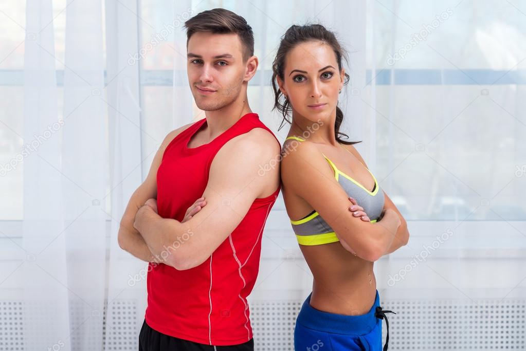 athletic sporty couple friends woman and man trainers or coach client in sport hall gym standing arms crossed sportsmen professionals looking at camera