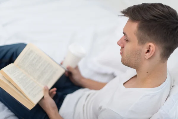 Мужчина читает книгу на кровати дома — стоковое фото