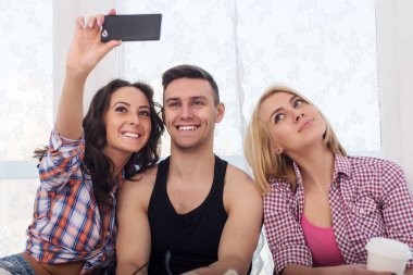 Happy friends two women and man taking selfie with camera or smartphone together wearing summer clothes  jeans shorts jeanswear street urban casual style having fun.