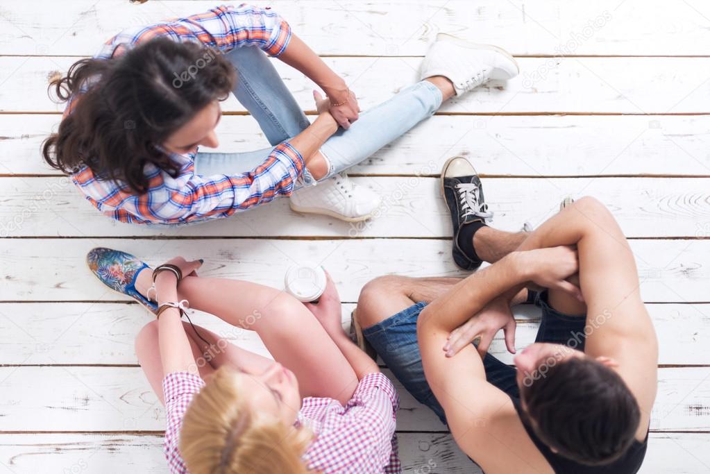 Friends two girls and guy sitting on floor in summer jeanswear street urban casual style talking, having fun, top view