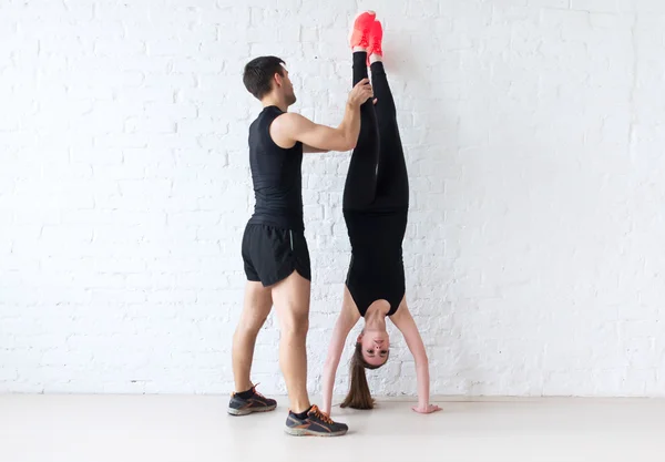 Vrouw sportman doen een handstand tegen mannelijke trainer betonnen wand helpen haar concept sport, fitness, lifestyle en mensen — Stockfoto