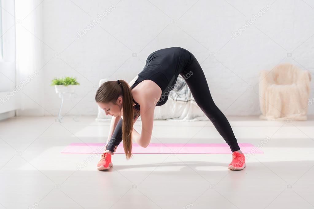 Athletic woman doing stretching exercise her hamstrings and back forward  bend lean down aerobics or warming up with gymnastics at home Stock Photo  by ©undrey 72893181