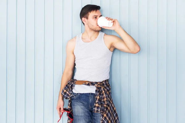 Retrato jovem segurando copo de papel e beber café da cidade casual estilo urbano olhando para a câmera de pé perto da parede de madeira . — Fotografia de Stock