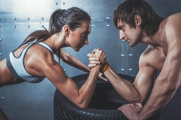 Atleet gespierde sporters man en vrouw met handen geklemd arm worstelen uitdaging tussen een jong koppel crossfit fitness sport opleiding levensstijl bodybuilding-concept. — Stockfoto