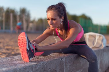 Fitness modeli atlet kız onun hamstrings, sırt ve bacak germe kadar sıcak. Açık havada plaj veya spor yere yaz akşam adlı müzik kulaklık ile egzersiz genç kadın