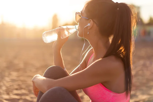 Nádherné fitness atlet žena pitné vody po práci se cvičit na letní večer při západu slunce v pláž venkovní portrét. — Stock fotografie