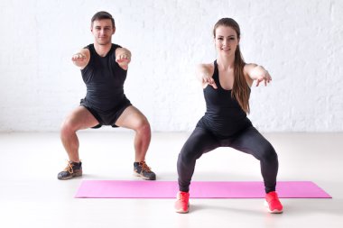Fitness man and woman exercising squat exercise hands behind head looking at camera concept sport, training, warming up lifestyle clipart