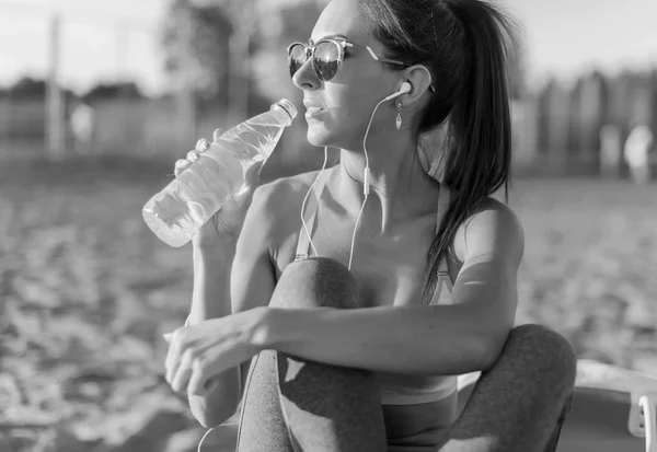 Hermosa atleta de fitness mujer bebiendo agua después de hacer ejercicio en verano en la playa retrato al aire libre . — Foto de Stock