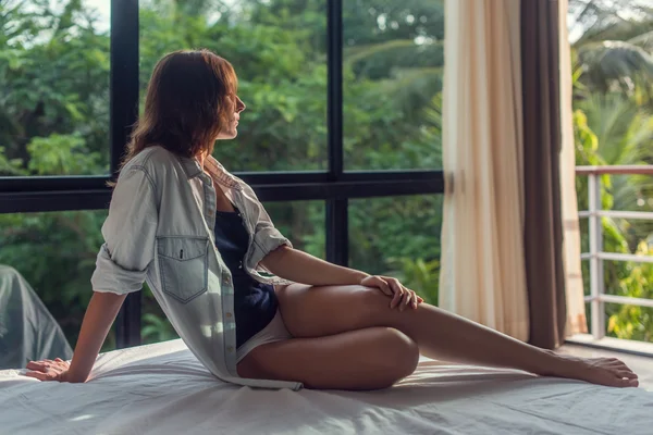 Hermosa joven está acostada en el mal y mirando a través de las ventanas. Linda dama viendo maravillosa terraza con vista —  Fotos de Stock