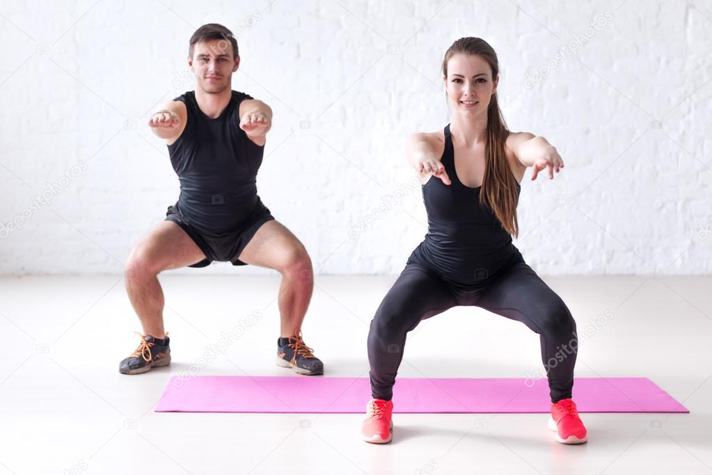 Fitness man and woman exercising squat exercise hands behind head looking at camera concept sport, training, warming up lifestyle