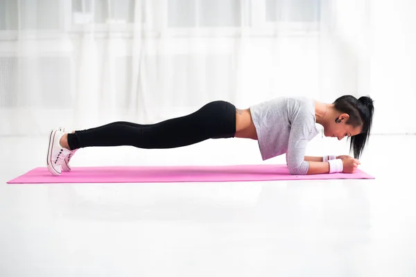 Slim fit girl doing planking core muscles exercise indoors at home in the living room side view fitness healthy lifestyle and diet concept — ストック写真