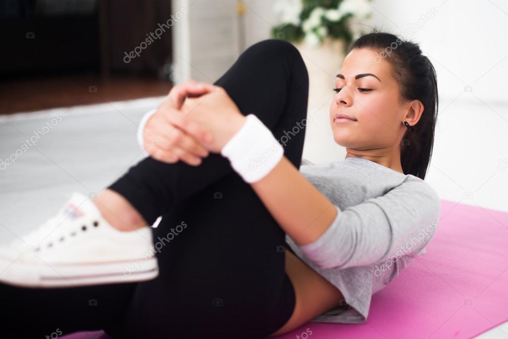 Fit woman doing aerobics gymnastics stretching exercises her leg lying on back warm up at home yoga mat.