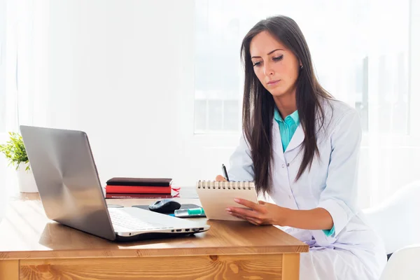 Porträtt av läkare som arbetar på hennes kontor skriva recept sitter arbetsplatsen. — Stockfoto