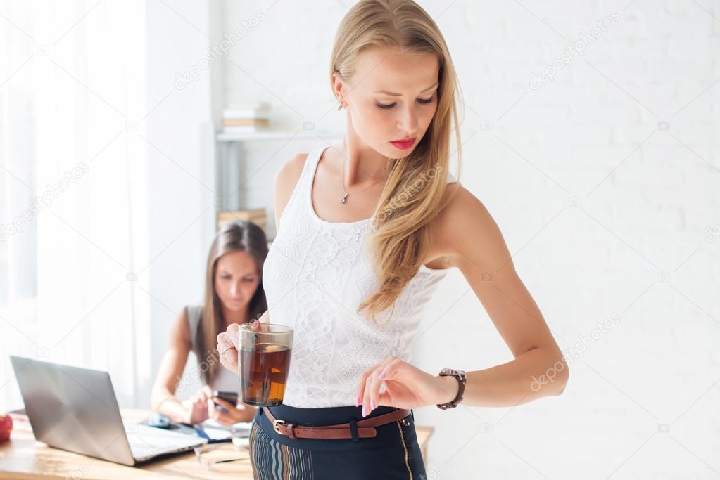 Portait of beautiful successful business woman looking at the time on her wrist watch holding cup coffee