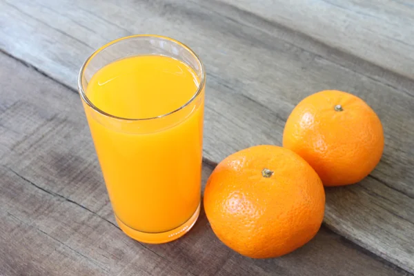 Vers oranje fruit geplaatst op houten vloer en SAP in glas — Stockfoto