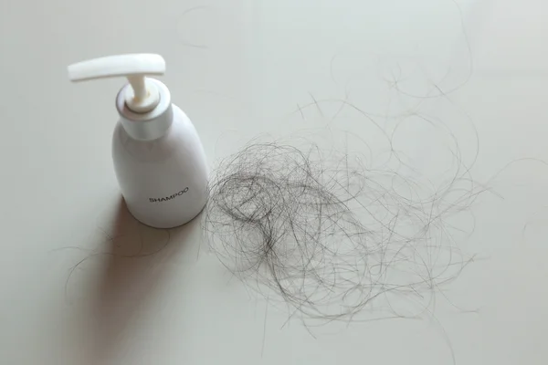 Bottiglia bianca di shampoo e perdita di capelli su tessuto bianco . — Foto Stock