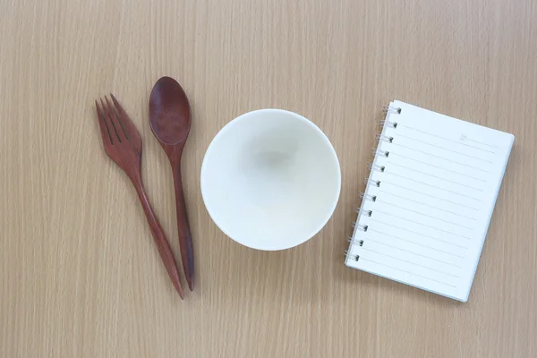Keukengerei en nota boek over houten achtergrond. — Stockfoto