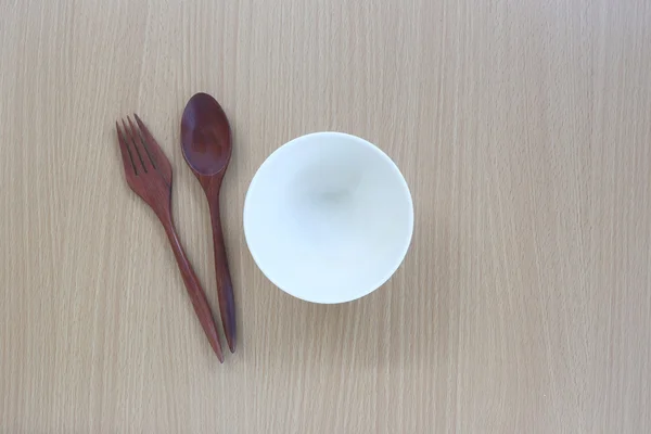 Houten lepel, vork en witte cup in bovenaanzicht op houten achtergrond. — Stockfoto