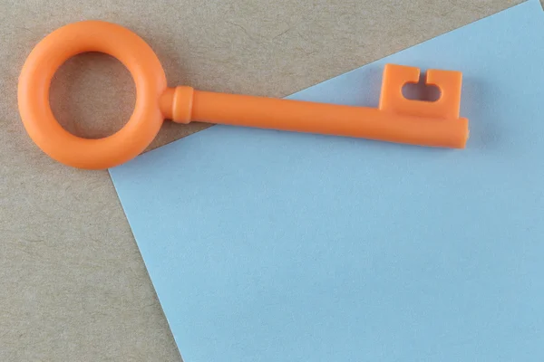 Llave de plástico naranja se coloca en la nota de papel azul . —  Fotos de Stock