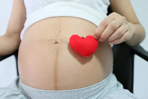 Rotes Herzsymbol in der Hand einer schwangeren Asiatin. — Stockfoto