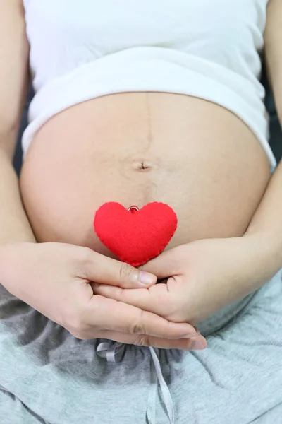Cuore rosso simbolo in mano una donna asiatica incinta . — Foto Stock