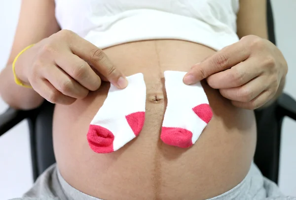 Έγκυες γυναίκες κρατήσει κάλτσα τοποθετείται στην κοιλιά. — Φωτογραφία Αρχείου
