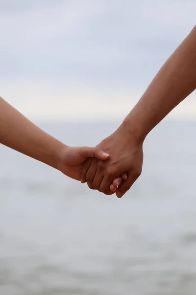 Young people holding hands on calm sea background for design in valentine and couple concept.