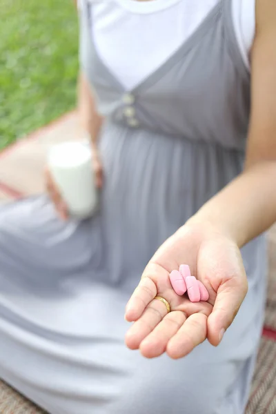 Zwangere vrouwen hebben een glas melk en vitamine pil in de hand te — Stockfoto