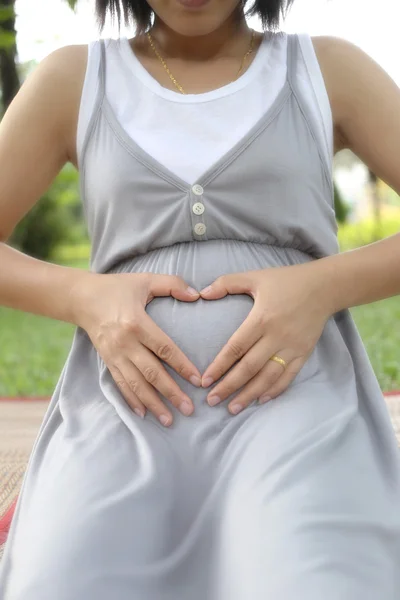 Mulheres grávidas colocam sua mão em sua barriga em forma de coração . — Fotografia de Stock