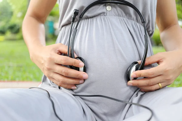 Les femmes enceintes mettent un écouteur à la main sur son ventre . — Photo