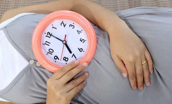 妊娠中の女性は、時間を伝える彼女の腹に時計を表示. — ストック写真