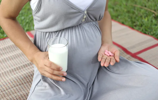 Pregnant women have a glass of Milk and vitamin pill in hand to