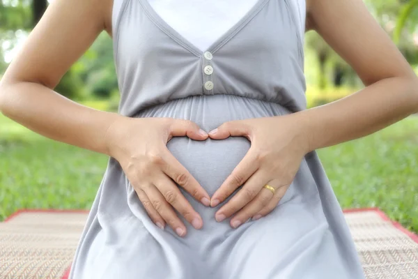 Kobiety w ciąży położyć rękę na jej brzuch kształt serca. — Zdjęcie stockowe