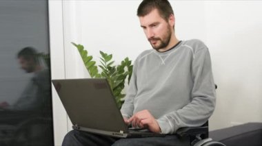 Dizüstü bilgisayarlı tekerlekli sandalyedeki genç adam.