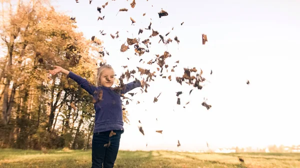 Усміхнена дівчина кидає сухе листя — стокове фото