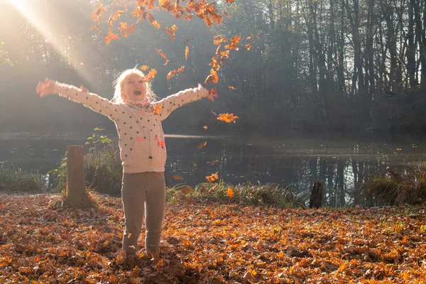 Dziecko rzucające suche liście jesienią — Zdjęcie stockowe