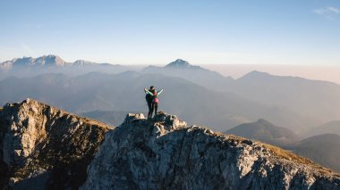 İki kaşif zaferle bir dağın zirvesinde duruyor, şafak vakti uzak aralıklarda nefes kesen manzaranın tadını çıkarıyorlar..